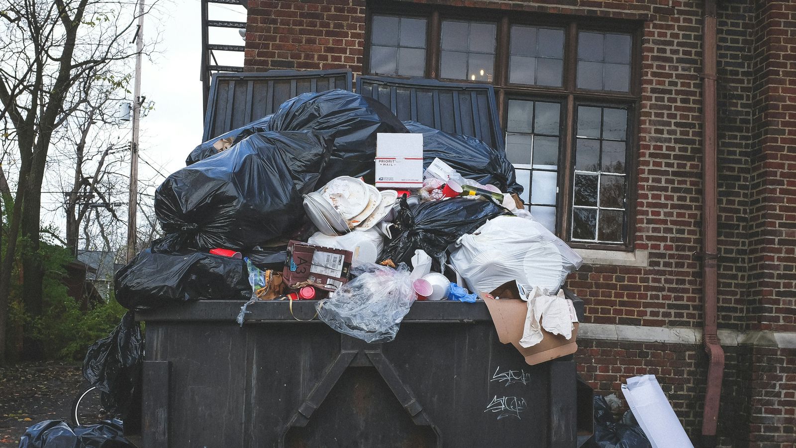 Voller Abfallcontainer hinter einem Gebäude vor der Entsorgung